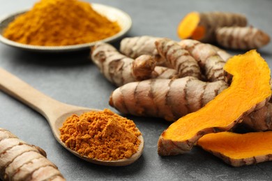 Photo of Aromatic turmeric powder and raw roots on grey table, closeup