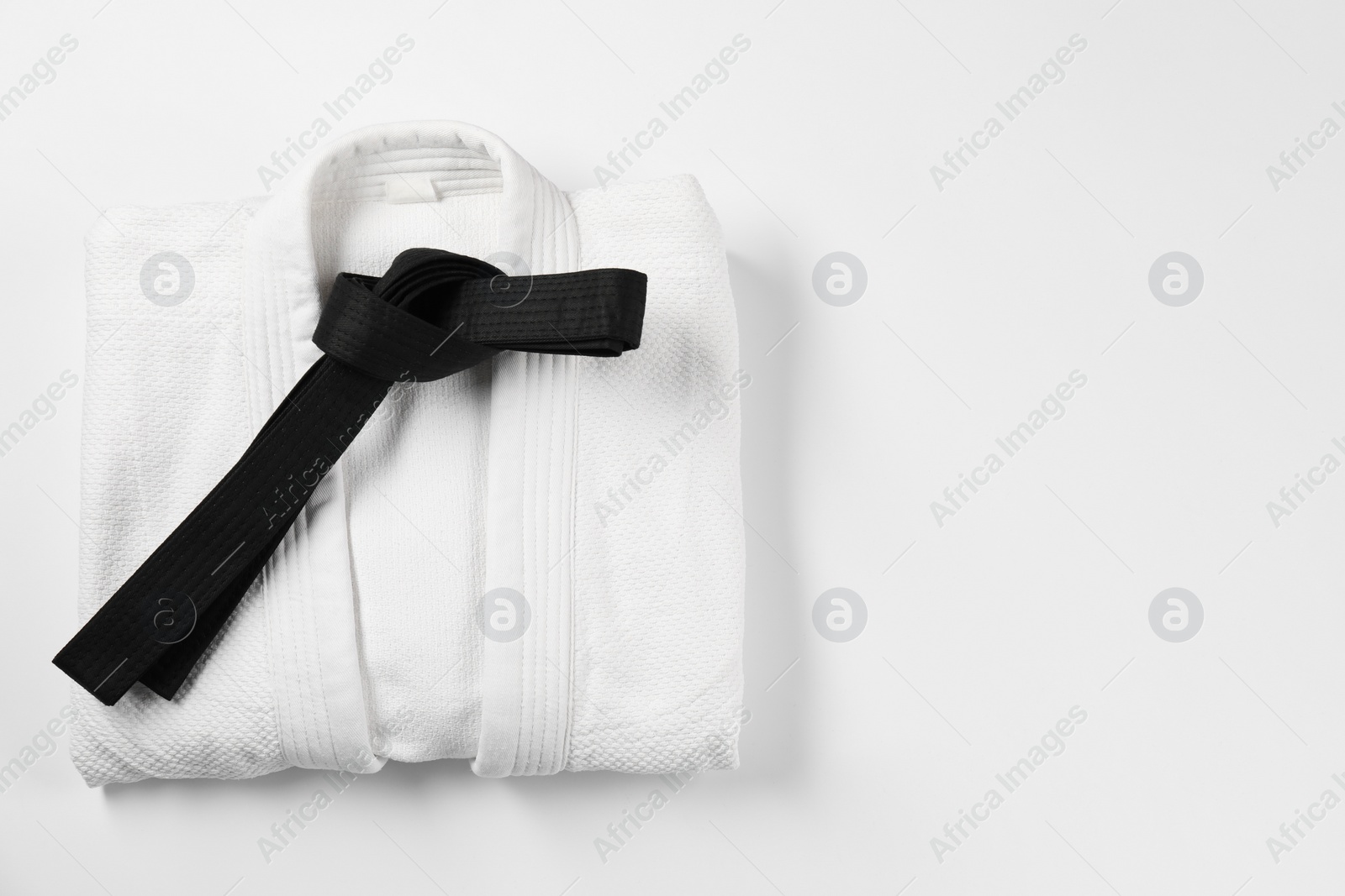 Photo of Black karate belt and kimono on white background, top view. Space for text