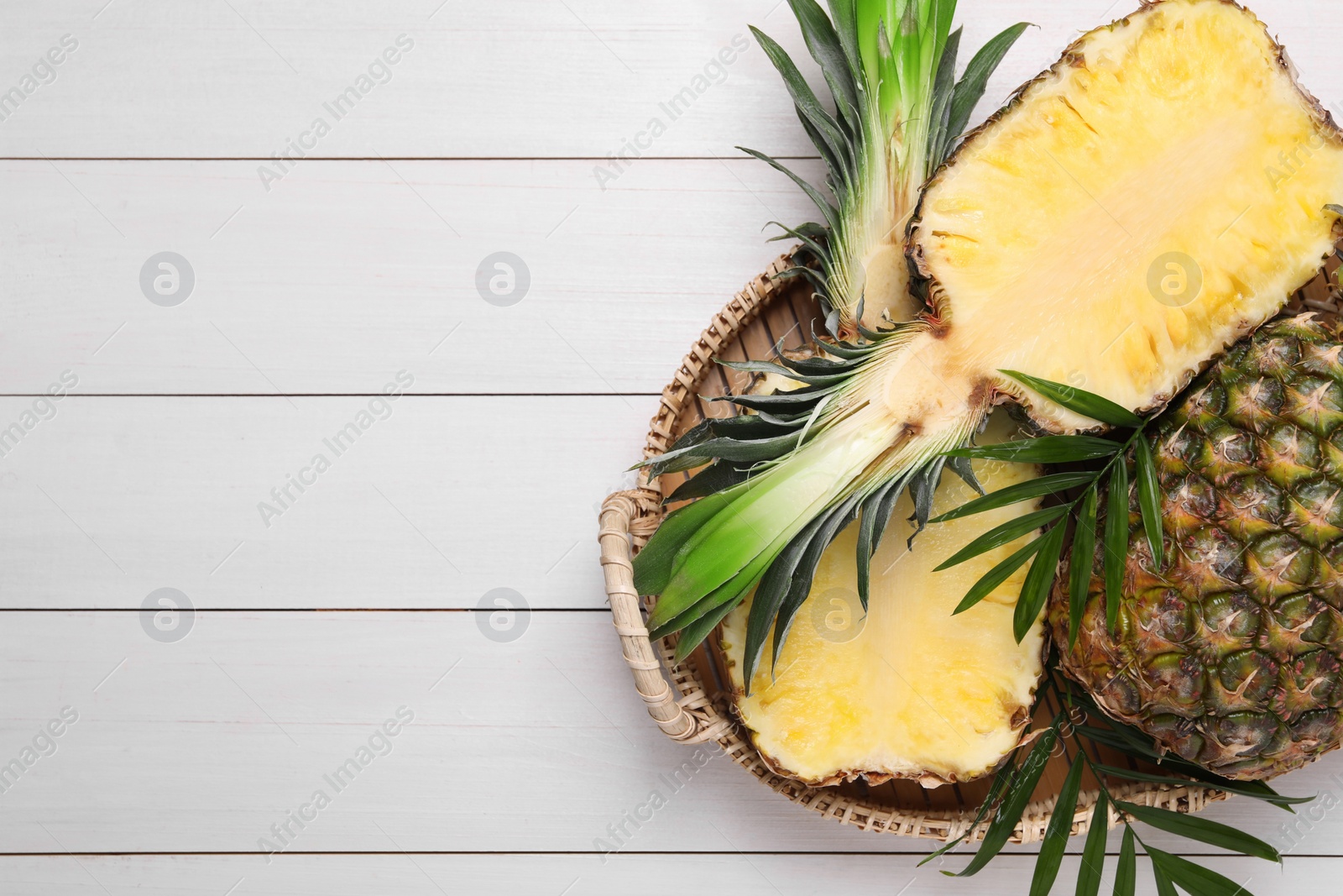 Photo of Whole and cut ripe pineapples on white wooden table, top view. Space for text