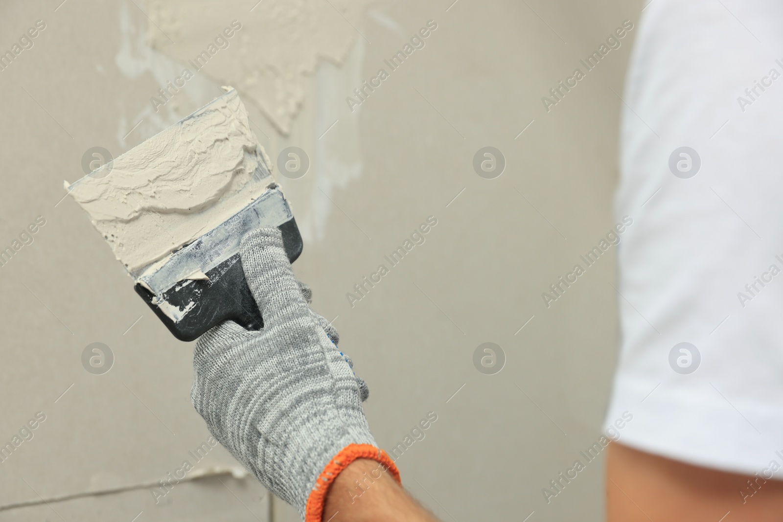 Photo of Worker plastering wall with putty knife, closeup