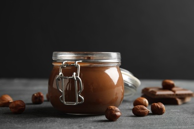 Photo of Composition with jar of tasty chocolate cream and hazelnuts on table against dark background