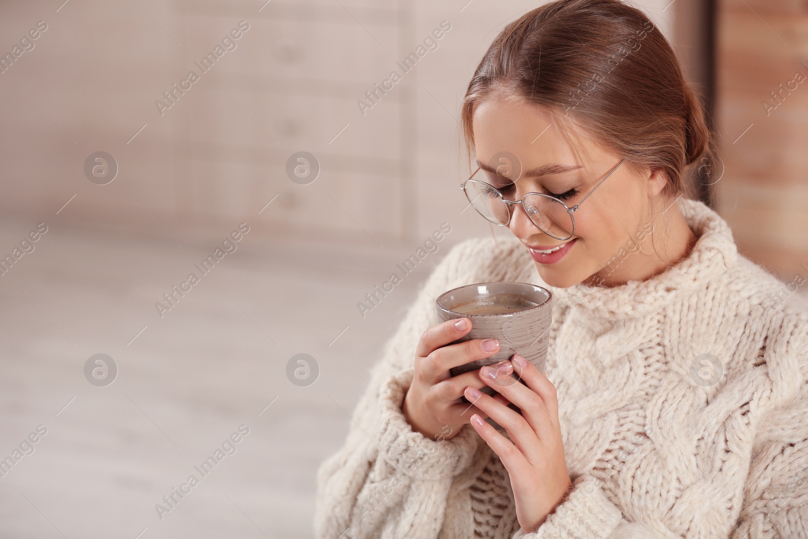 Photo of Beautiful young woman with cup of hot drink at home, space for text. Winter atmosphere