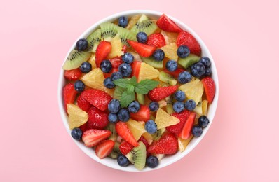 Photo of Yummy fruit salad in bowl on pink background, top view