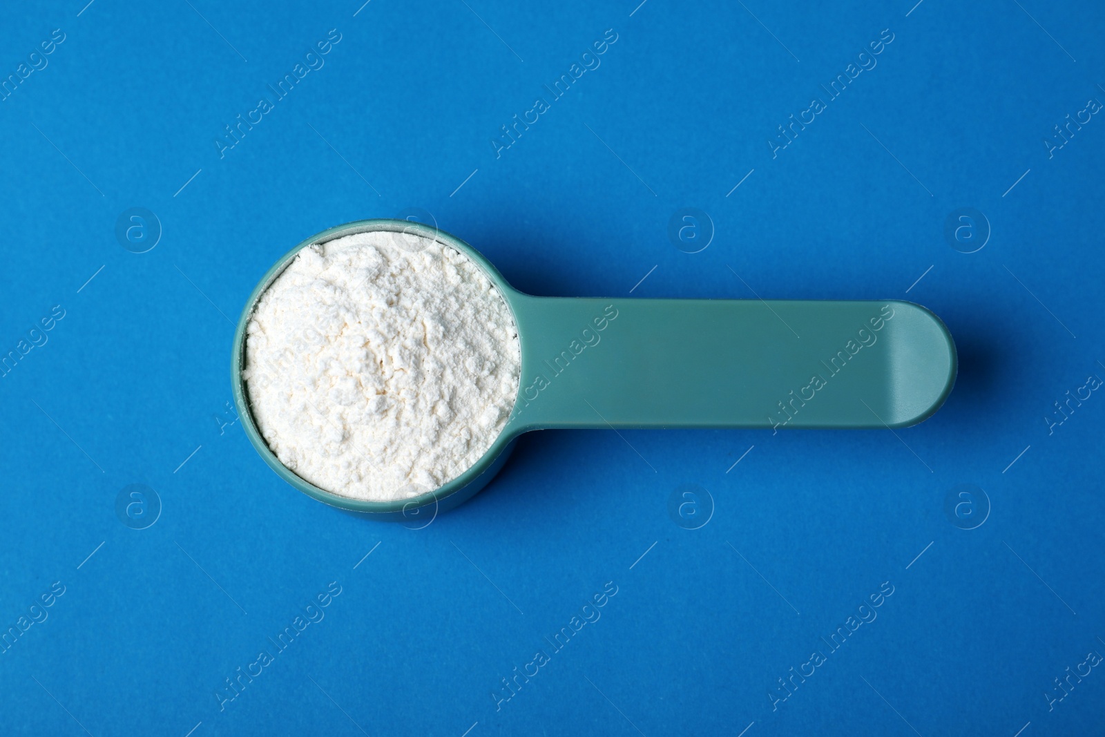 Photo of Scoop of protein powder on blue background, top view