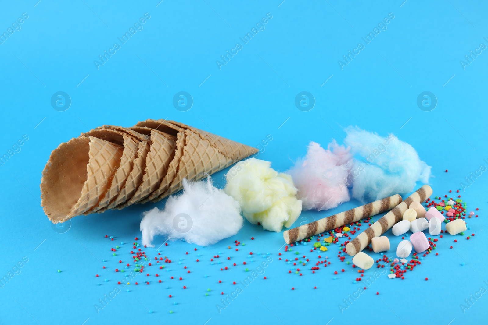 Photo of Sweet cotton candies, waffle cones, wafer sticks and marshmallows on light blue background