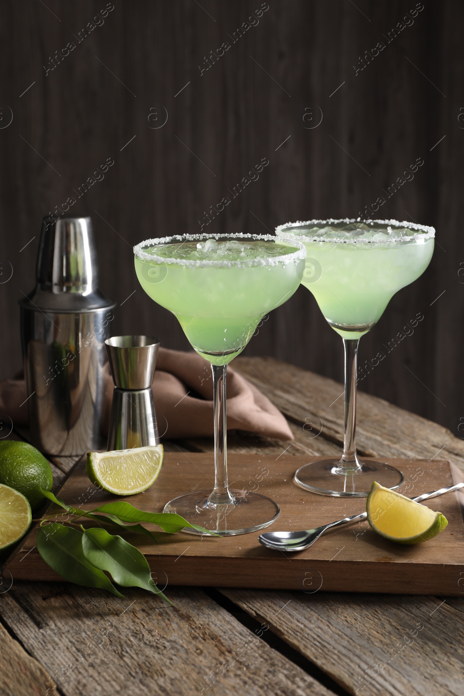 Photo of Delicious Margarita cocktail in glasses, limes and bartender equipment on wooden table