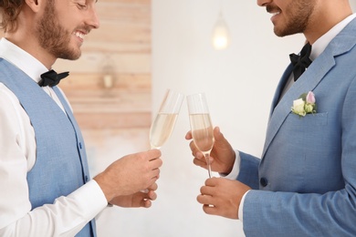 Photo of Happy newlywed gay couple with glasses of champagne at home