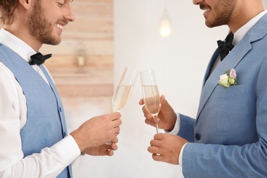 Happy newlywed gay couple with glasses of champagne at home