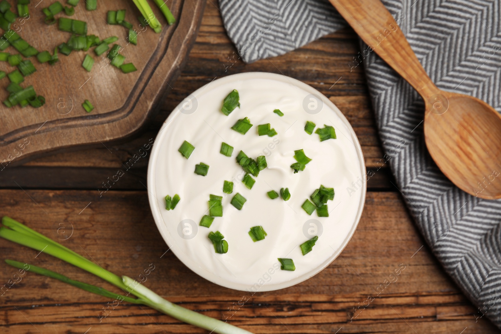 Photo of Fresh sour cream with onion on wooden table, flat lay