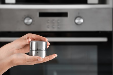 Photo of Woman holding kitchen timer near oven, closeup. Space for text