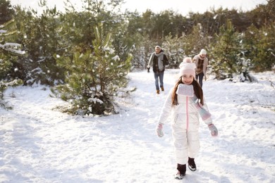 Photo of Cute little girl with her parents outdoors on winter day. Christmas vacation