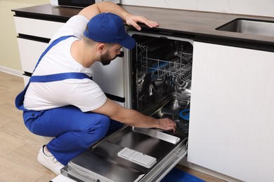 Serviceman repairing and examining dishwasher in kitchen