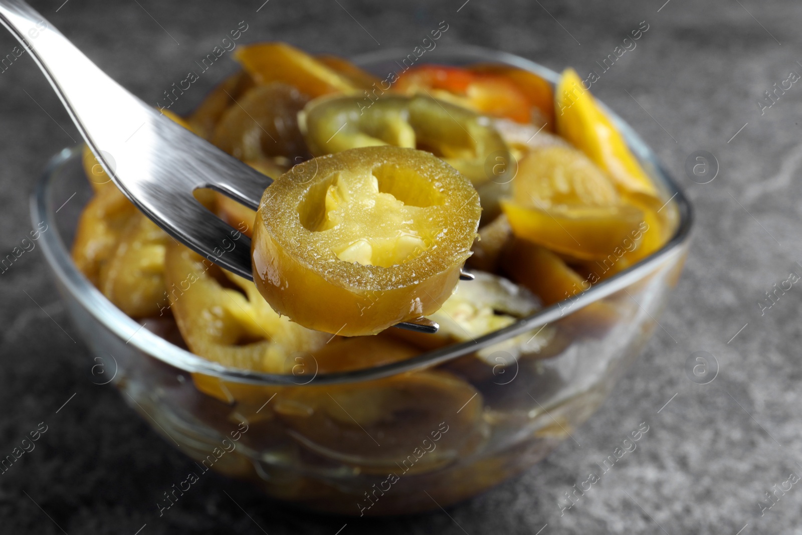 Photo of Fork with pickled green jalapeno near bowl on grey table, closeup