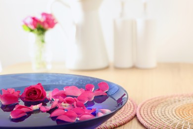 Photo of Pink roses and petals in bowl with water on table, closeup. Space for text