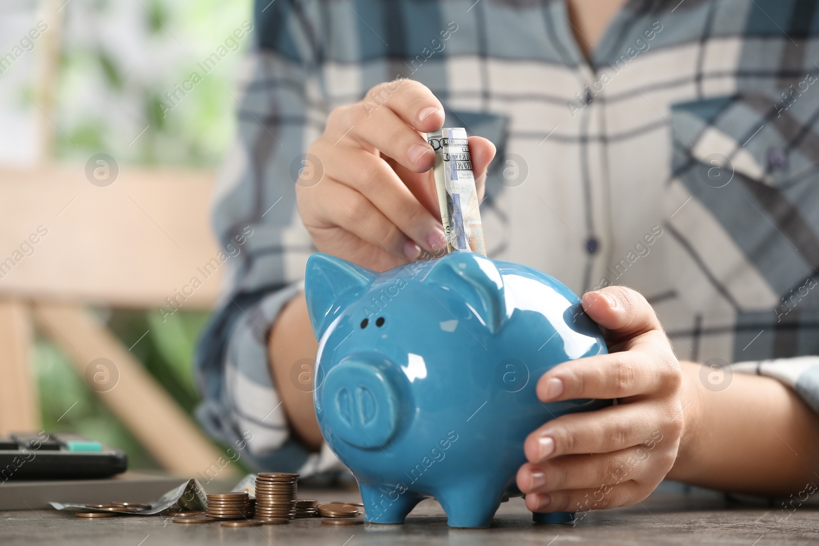 Photo of Woman putting money into piggy bank at table, closeup