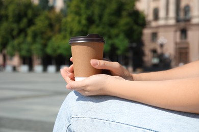 Photo of Woman holding takeaway cardboard coffee cup with plastic lid outdoors, closeup