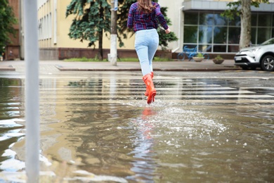 Photo of Woman with red rubber boots running in puddle, closeup. Rainy weather