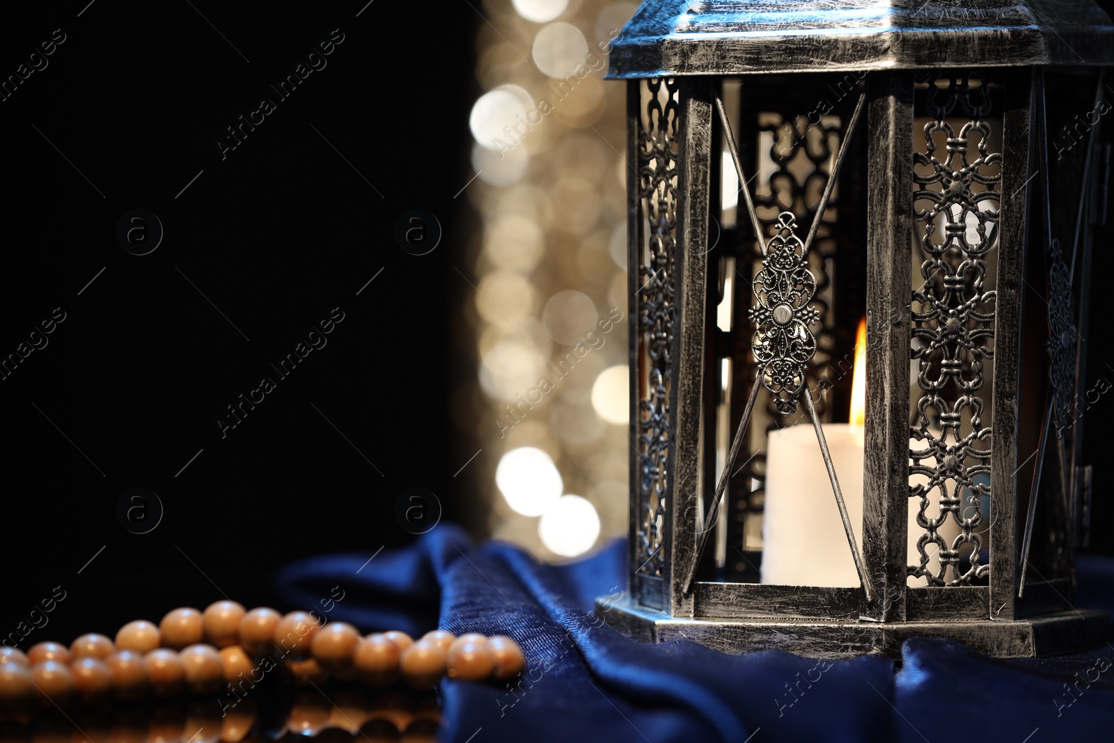 Photo of Arabic lantern and misbaha on table against blurred lights, closeup. Space for text