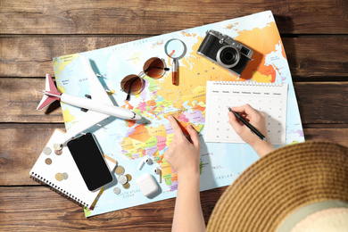 Photo of Woman marking calendar at table with world map, top view. Travel during summer vacation