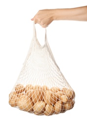 Photo of Woman holding mesh bag with raw fresh organic potatoes on white background, closeup