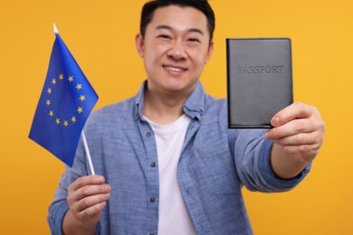 Photo of Immigration. Happy man with passport and flag of European Union on orange background, selective focus