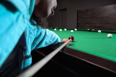 Young African-American woman playing billiard indoors, closeup