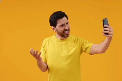 Emotional man taking selfie with smartphone on yellow background