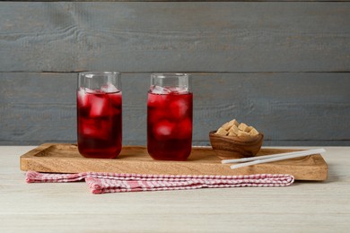 Photo of Delicious iced hibiscus tea, brown sugar cubes and straws on white wooden table
