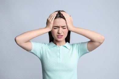 Photo of Young woman suffering from headache on light background