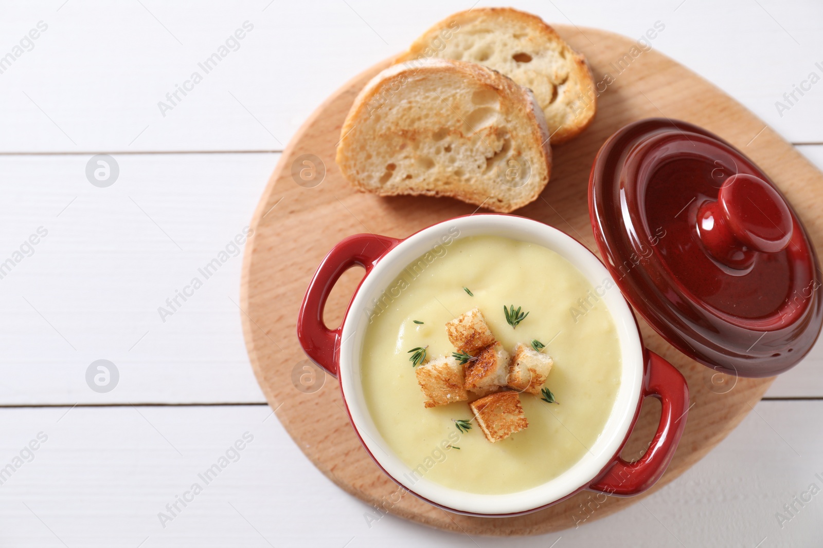 Photo of Tasty potato soup with croutons and rosemary in ceramic pot on white wooden table, flat lay. Space for text