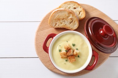 Photo of Tasty potato soup with croutons and rosemary in ceramic pot on white wooden table, flat lay. Space for text