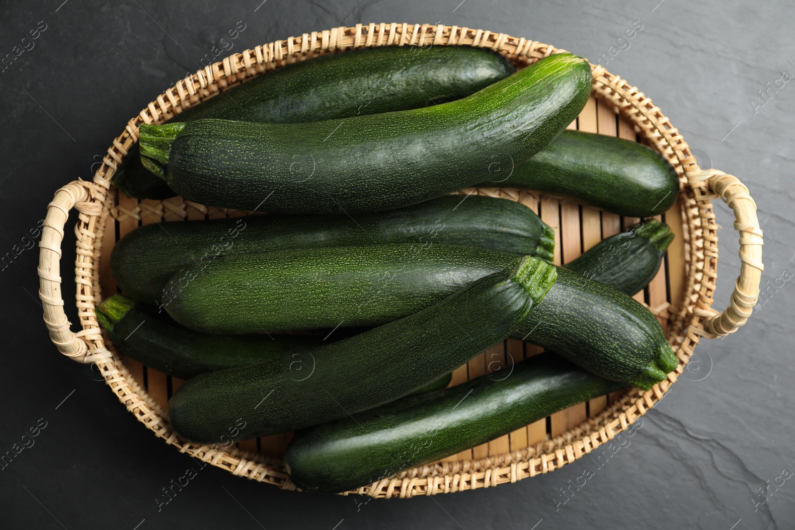 Photo of Basket with green zucchinis on black slate table, top view