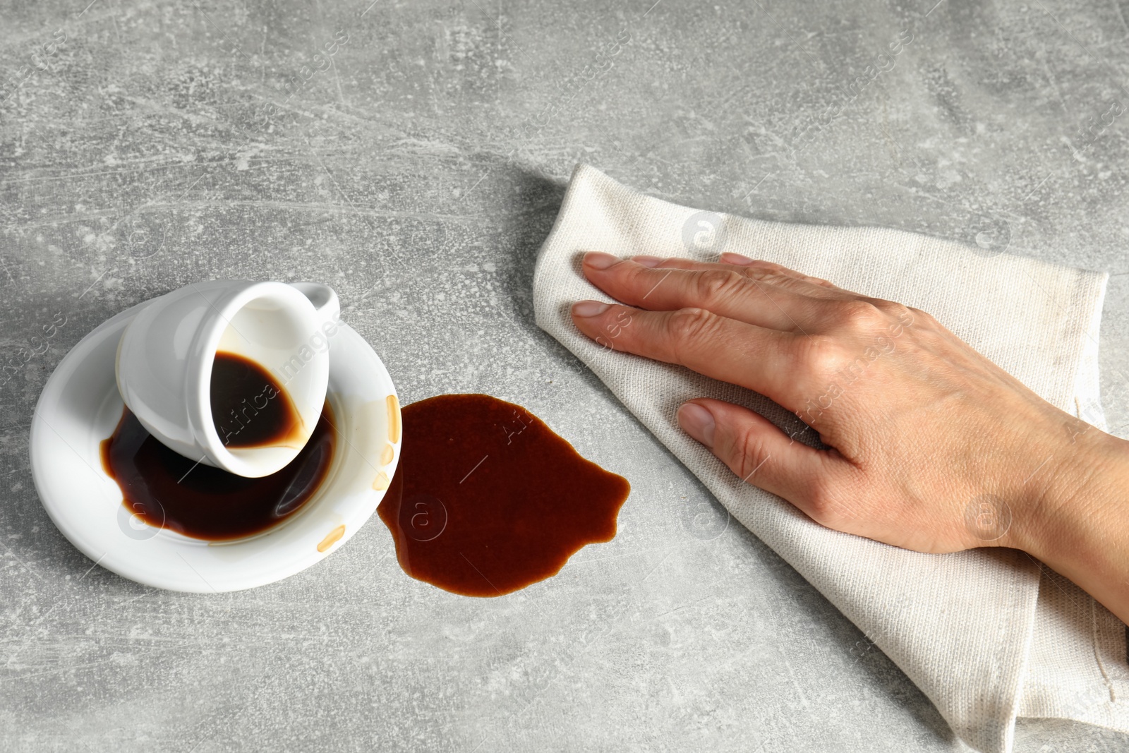 Photo of Woman wiping spilled coffee on grey table, closeup