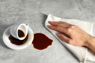 Photo of Woman wiping spilled coffee on grey table, closeup