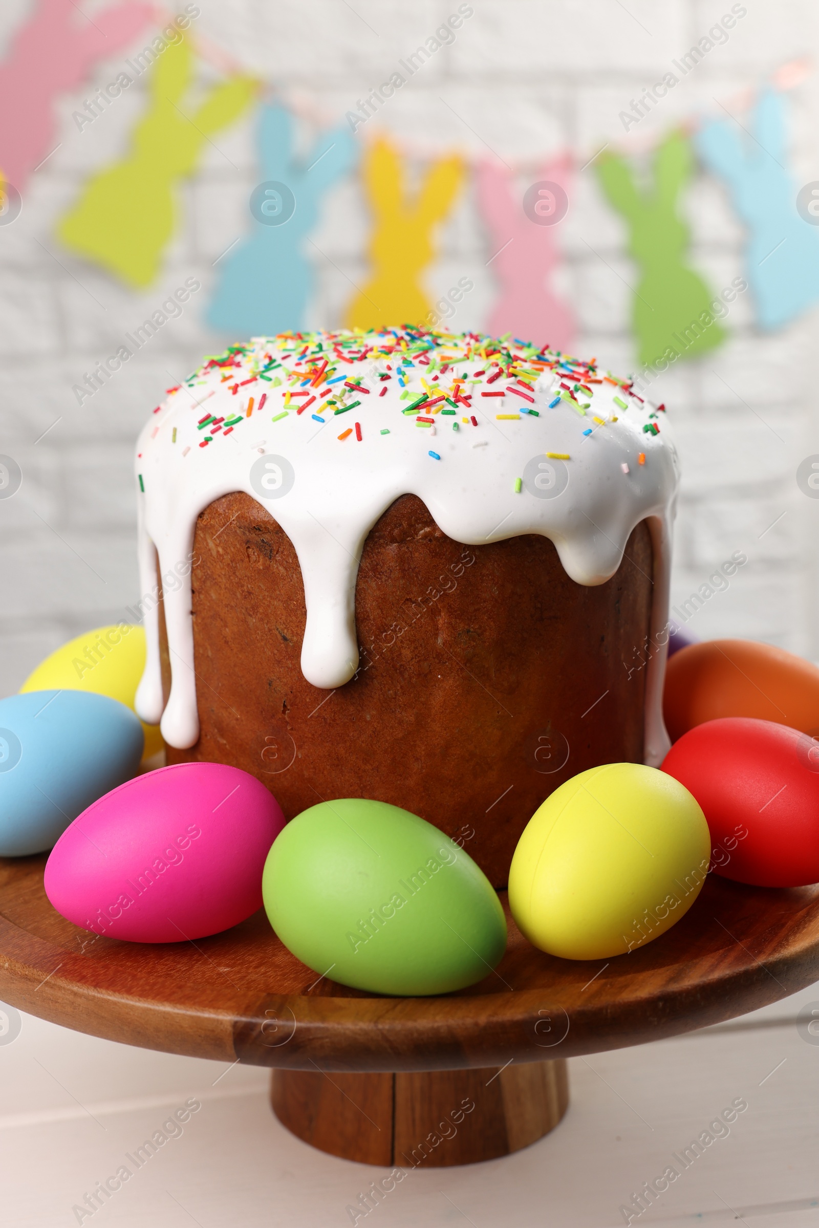 Photo of Stand with tasty Easter cake and decorated eggs on white wooden table