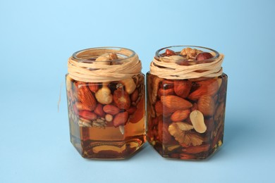 Jars with different nuts and honey on light blue background