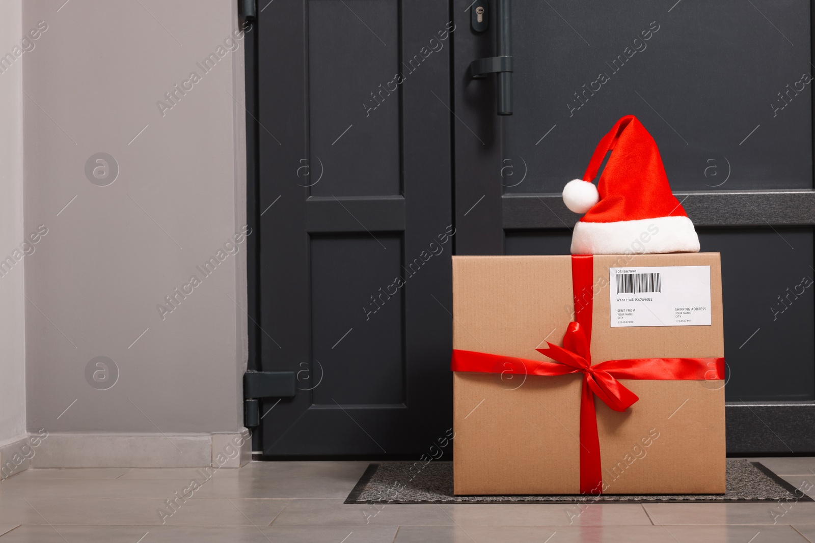 Photo of Christmas gift box and Santa hat near door indoors, space for text. Sending present by mail