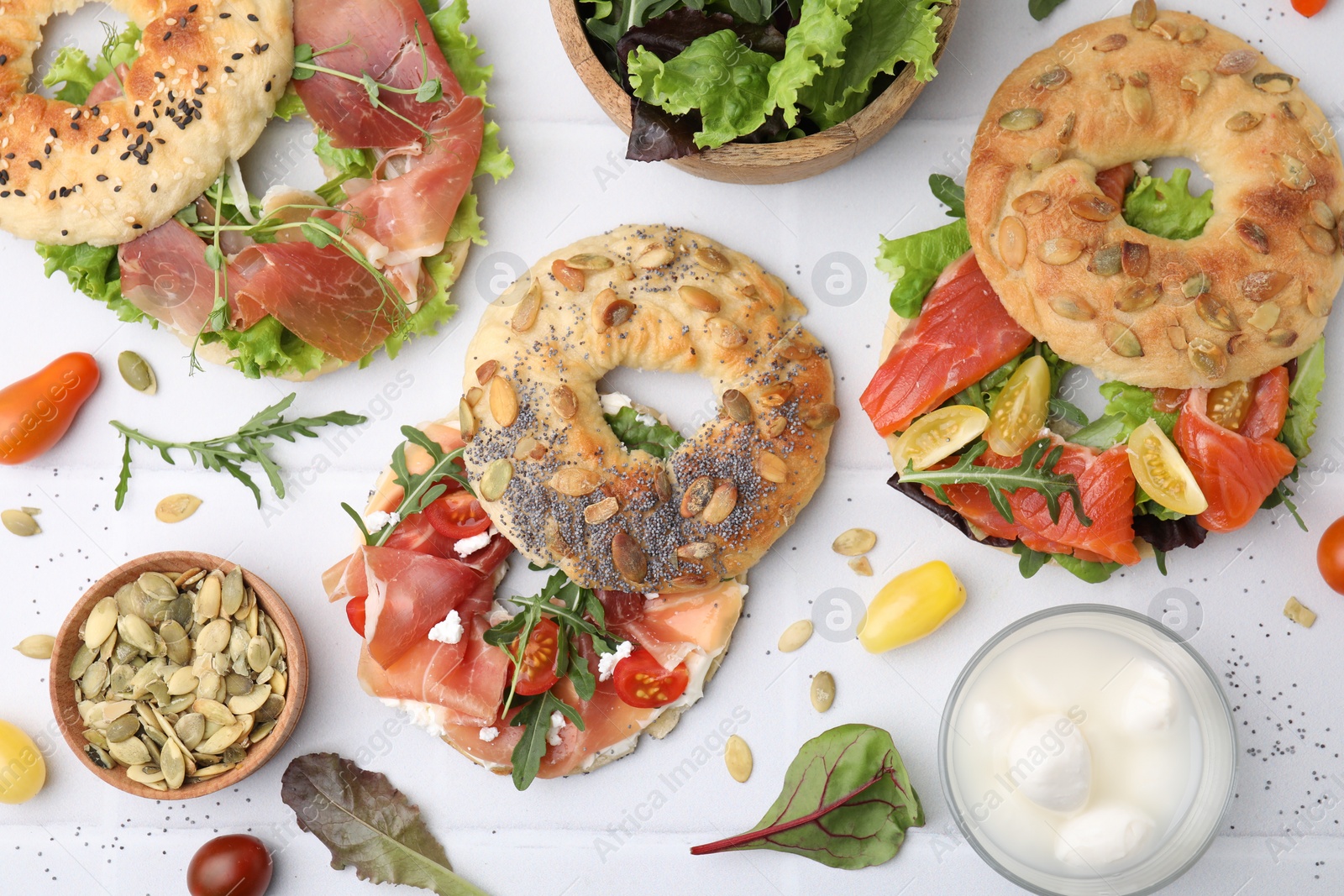 Photo of Tasty bagel sandwiches on white tiled table, flat lay