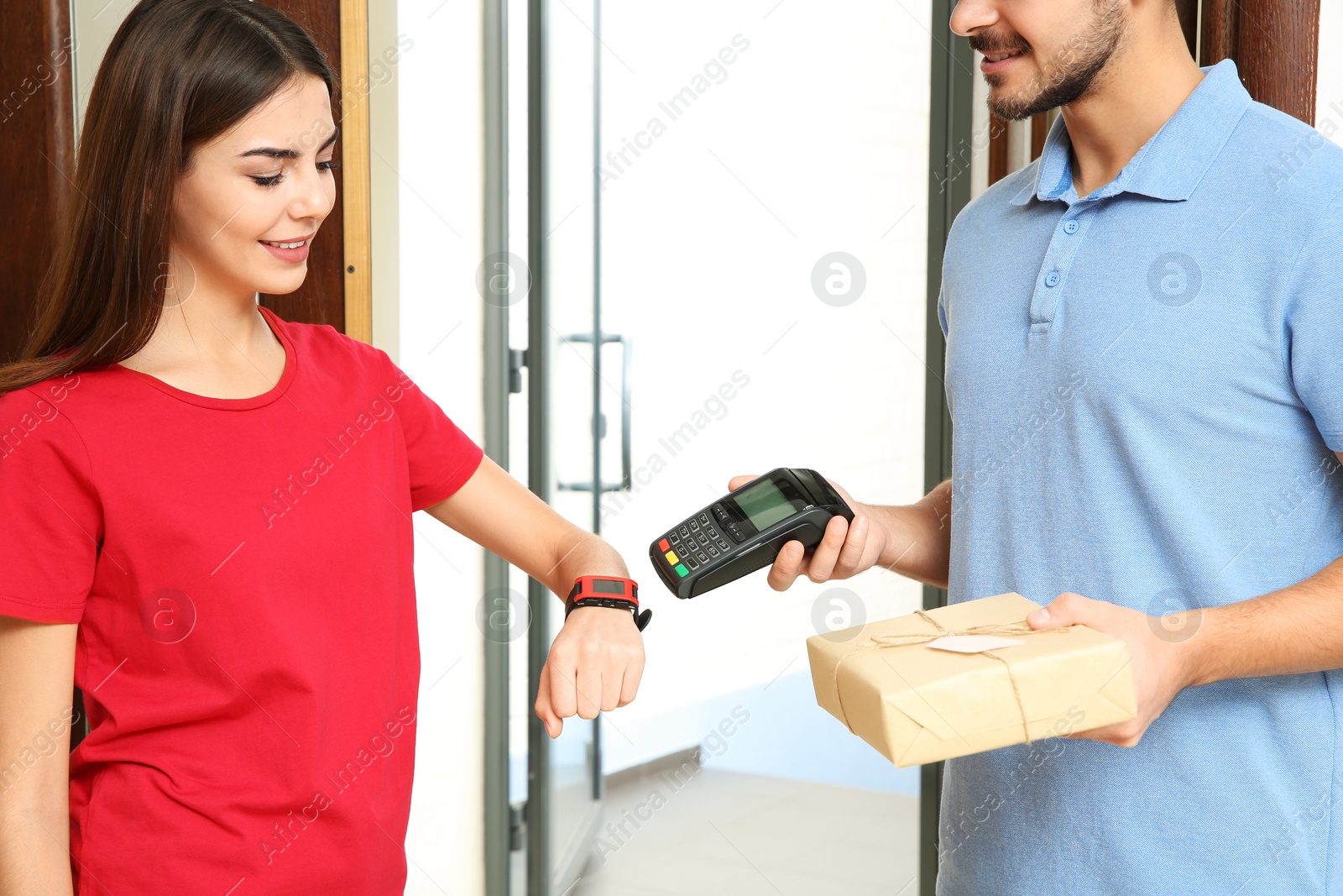 Photo of Woman with smartwatch using terminal for delivery payment indoors