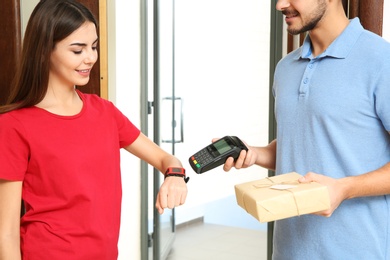 Photo of Woman with smartwatch using terminal for delivery payment indoors