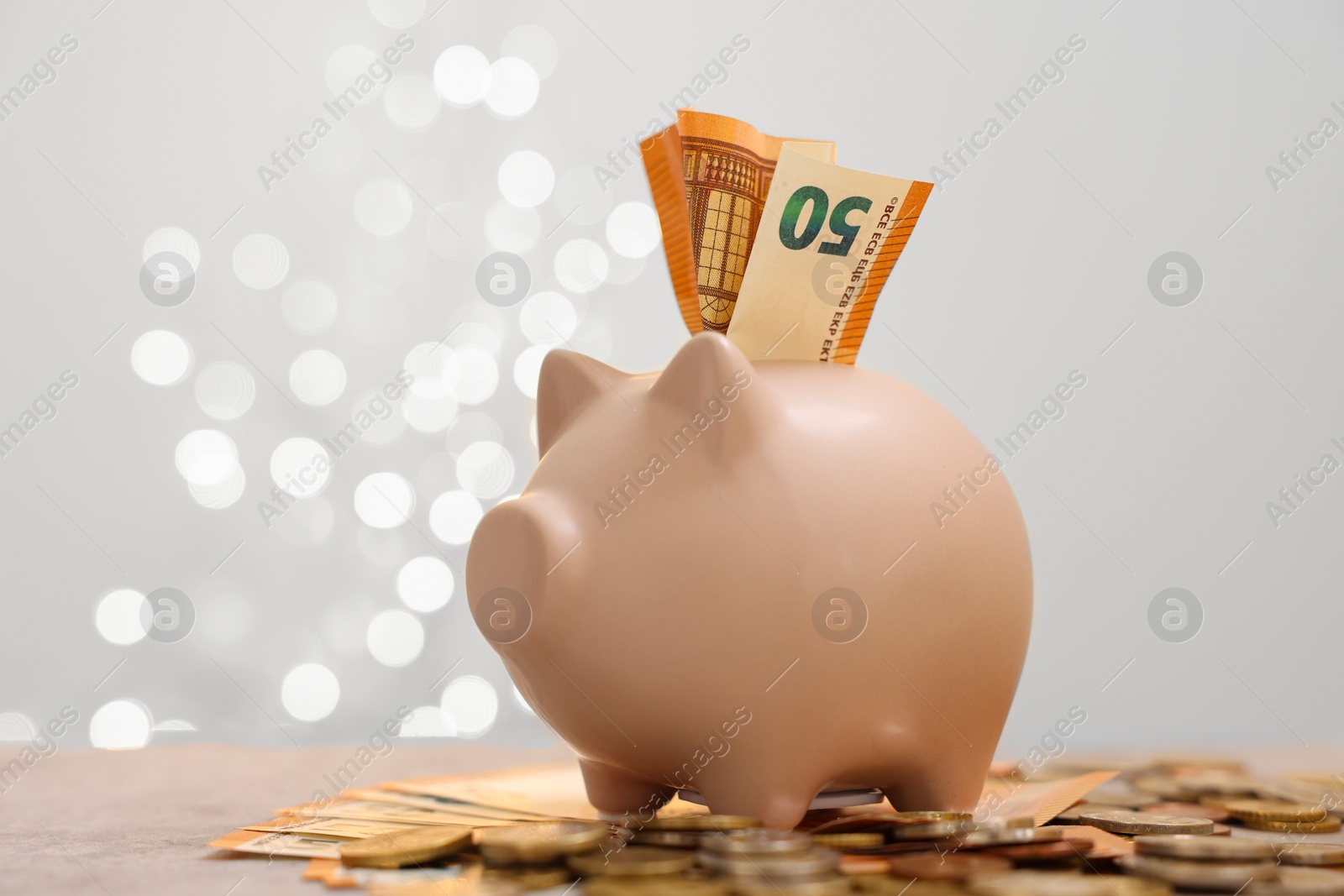 Photo of Piggy bank with euro banknote and coins on grey table against blurred lights