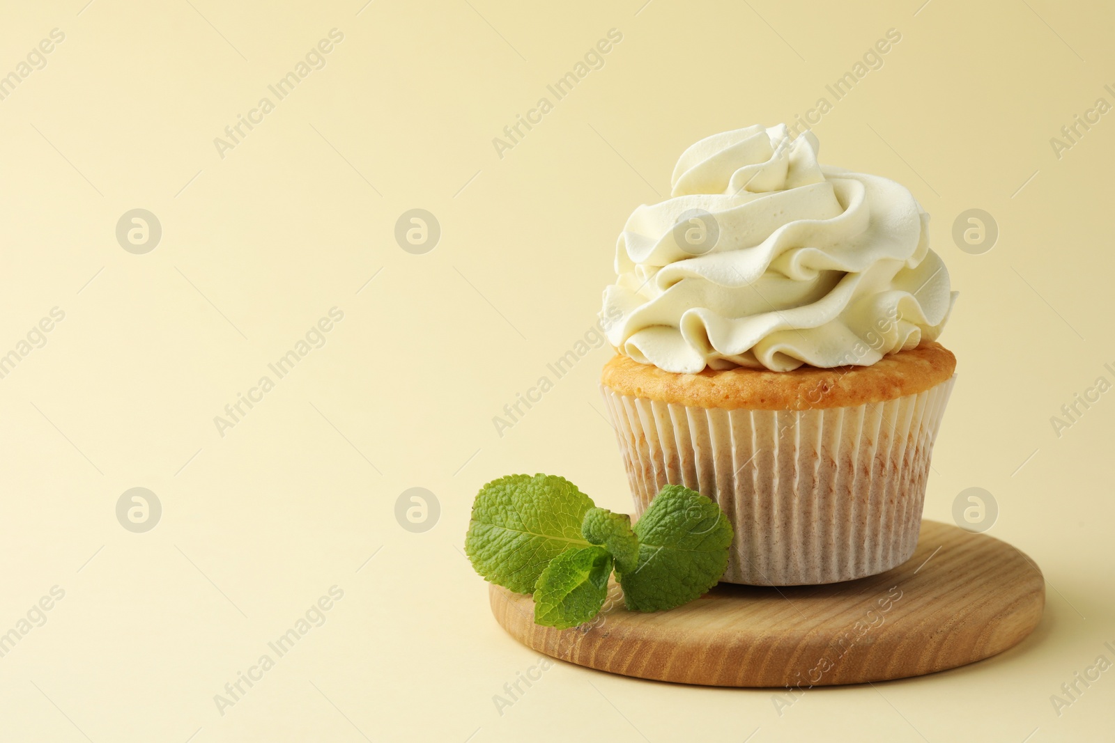 Photo of Tasty vanilla cupcake with cream and mint on pale yellow background, space for text