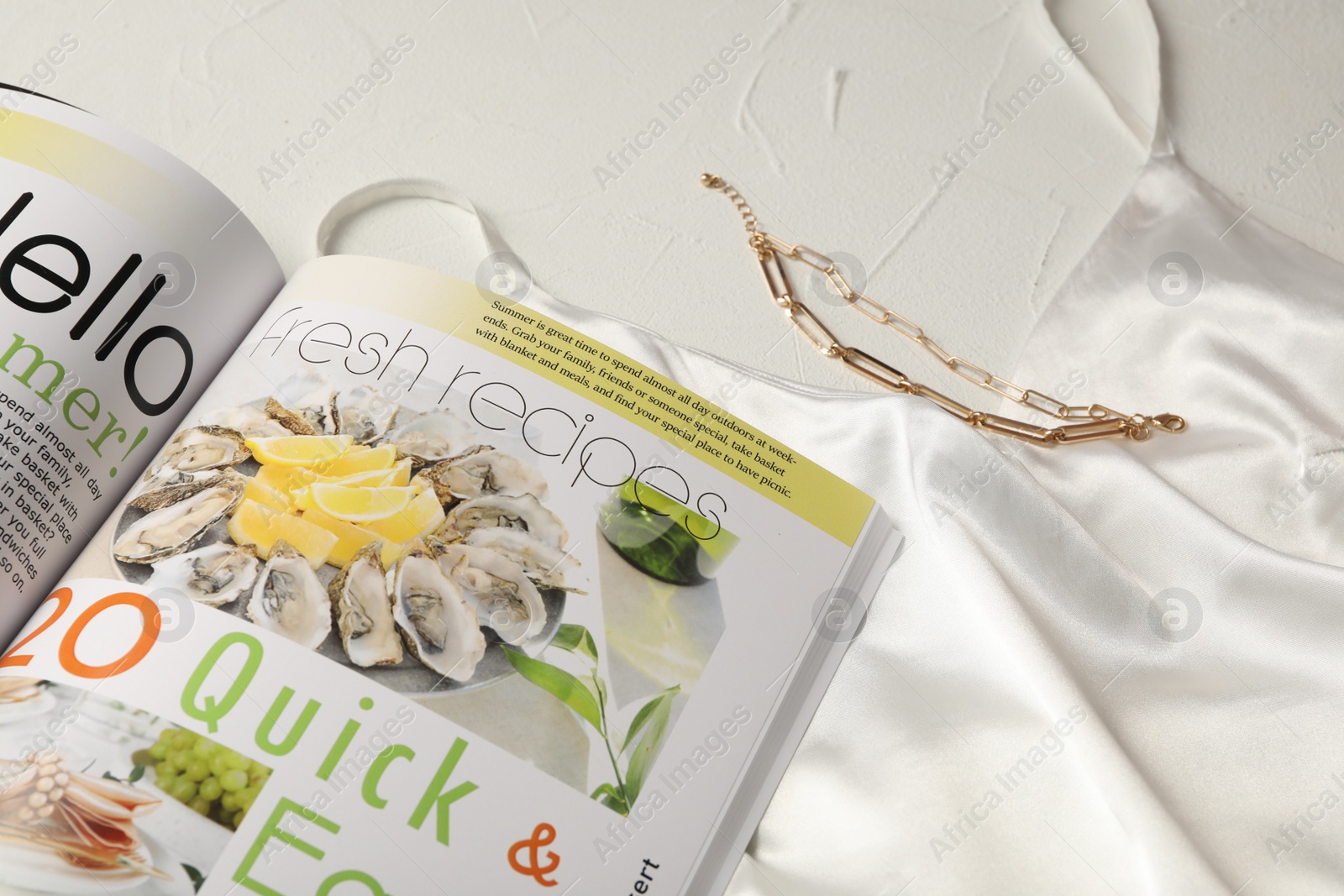 Photo of Open magazine, night dress and bracelet on white table