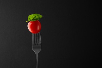 Fork with cherry tomato and basil on black background, space for text