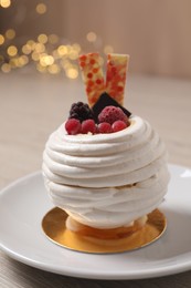 Photo of Delicious meringue dessert with berries on table against blurred lights, closeup