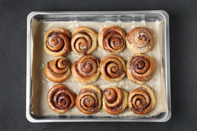Photo of Baking dish with tasty cinnamon rolls on dark table, top view