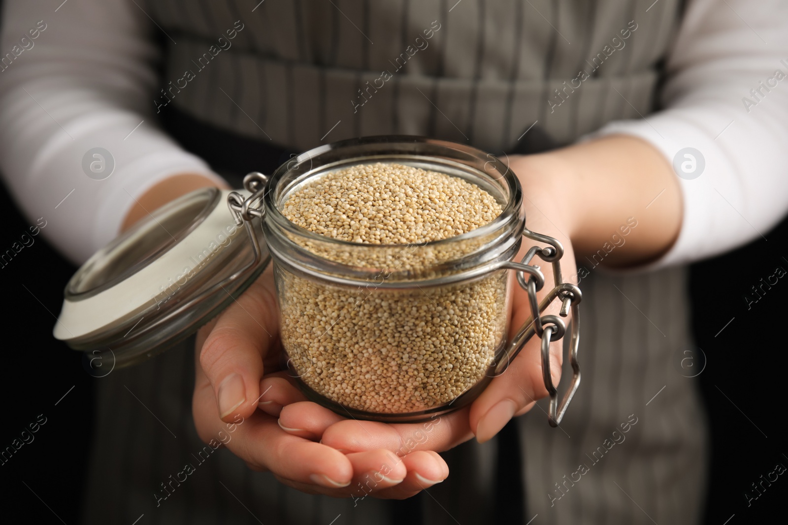 Photo of Woman holding jar with white quinoa on dark background, closeup