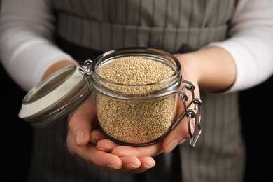 Woman holding jar with white quinoa on dark background, closeup