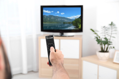 Image of Man switching channels on modern TV with remote control at home