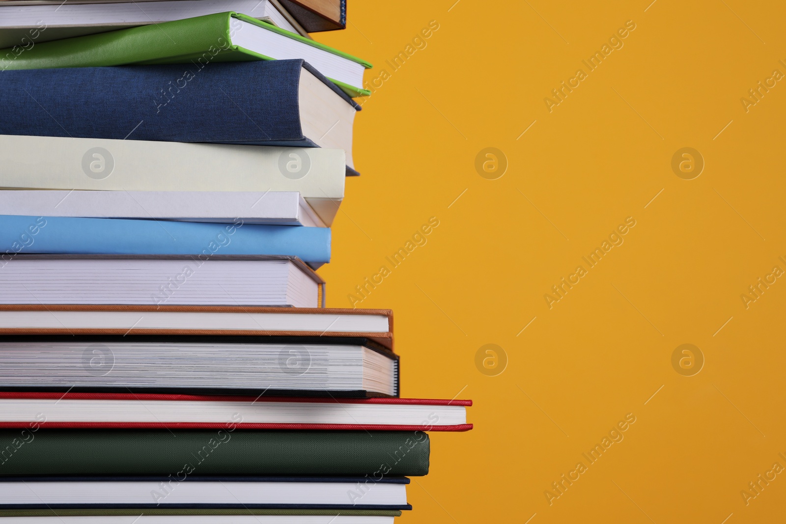 Photo of Stack of hardcover books on orange background, closeup. Space for text